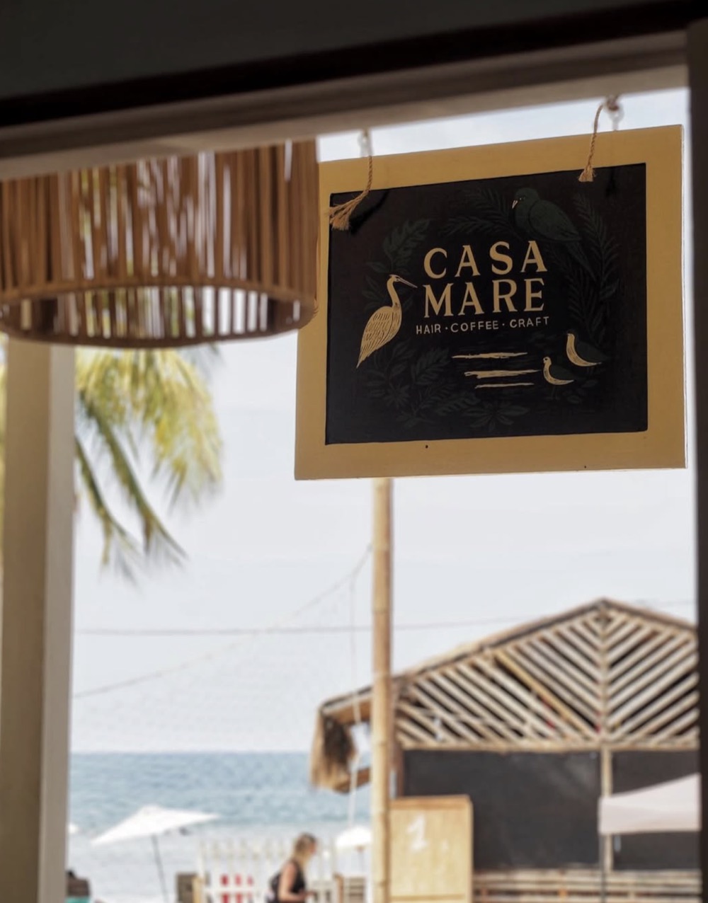 The Casa Mare sign — hair, coffee, craft — with the sea behind it