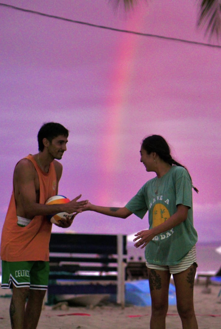 Two players shaking hands under a rainbow sky after a game